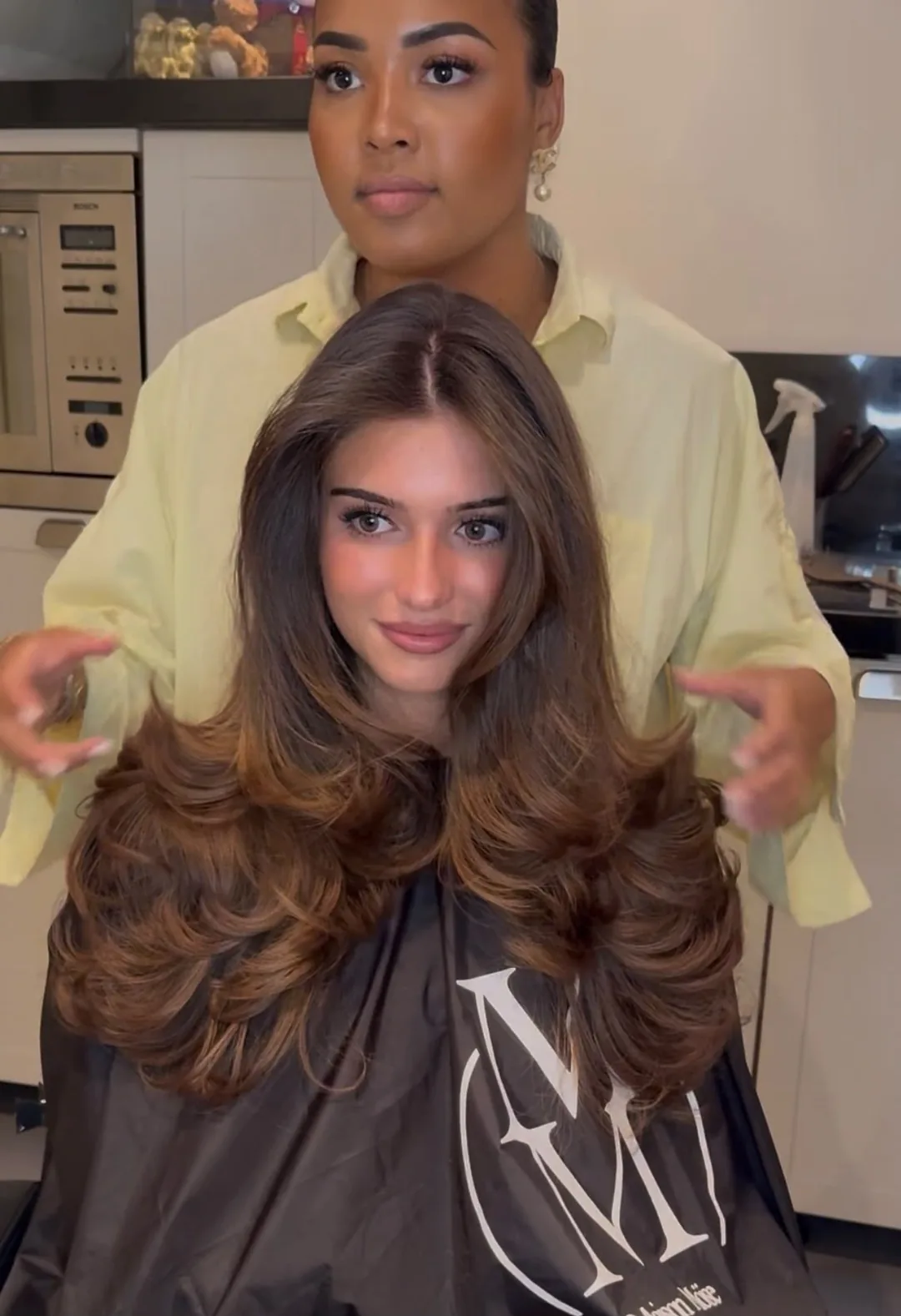 Klant met lang bruin haar in een volumineuze layered blowout, Moïse staat erachter